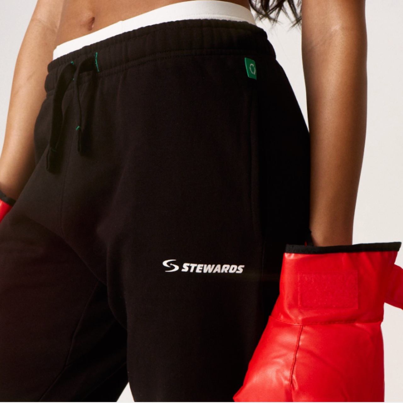 Person wearing black shorts with 'STEWARDS' logo and red boxing gloves on a light gray background